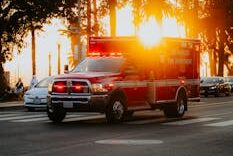 Fire department ambulance driving through city streets at sunset with palm trees in the background.