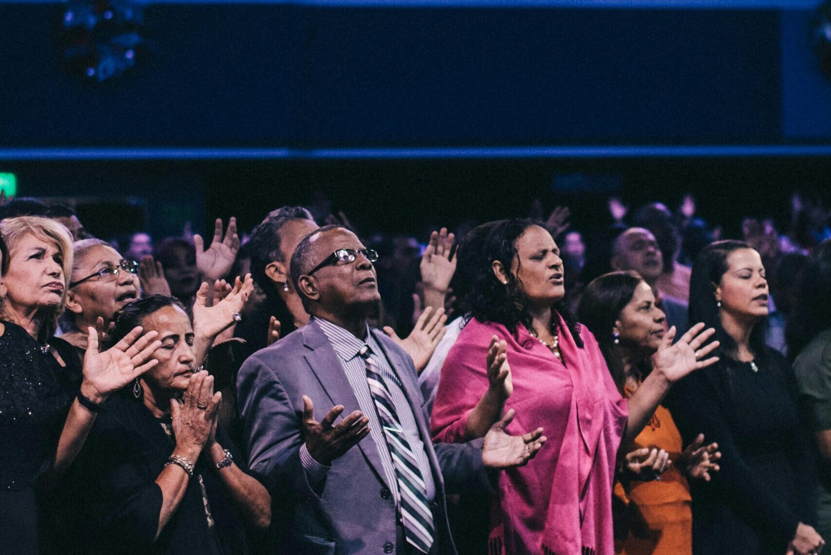 A diverse group of people participating in a lively worship event in a large auditorium.